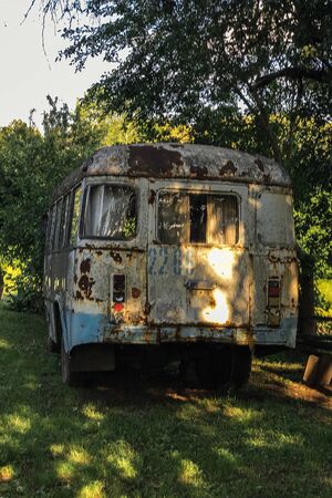 Old rusty soviet bus in a wild forest with an abandoned house.の写真素材