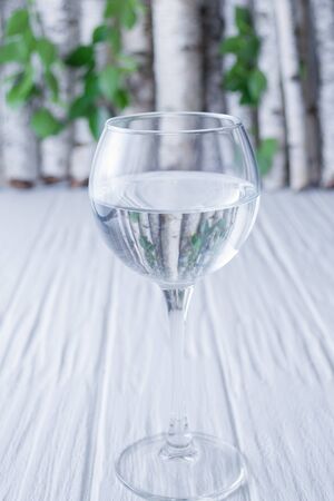 Water in a glass on a wooden background on a background of birch branches.の写真素材