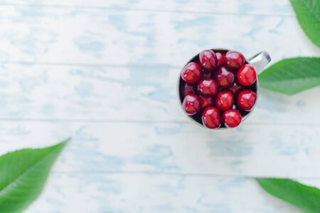 Cherries in a steel mug on a wooden background.の写真素材