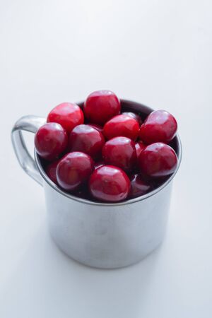 Sweet cherries in a steel mug on a white paper background.の写真素材