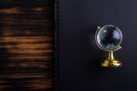 Glass globe on a black matte notebook on a wooden background.の写真素材