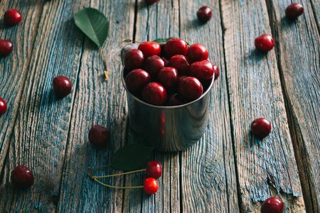 Cherries in a steel mug on a wooden background.の写真素材