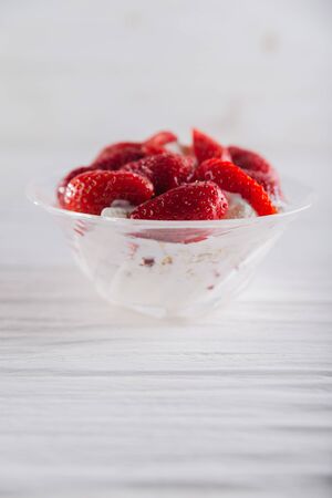 Strawberry dessert in a plate with ice cream and cream on a white wooden background.の写真素材