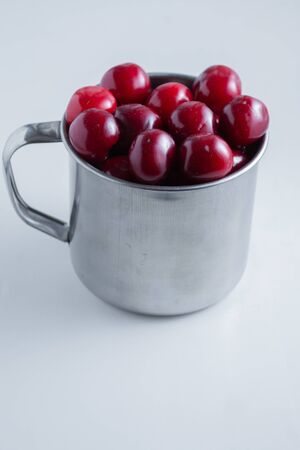 Sweet cherries in a steel mug on a white paper background.の写真素材