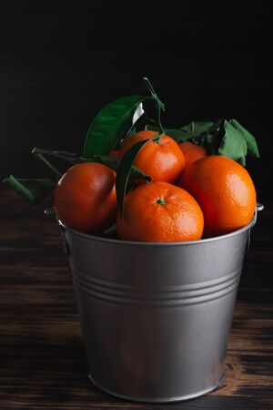 Fresh tangerines with leaves in a bucket on a wooden old background.の写真素材