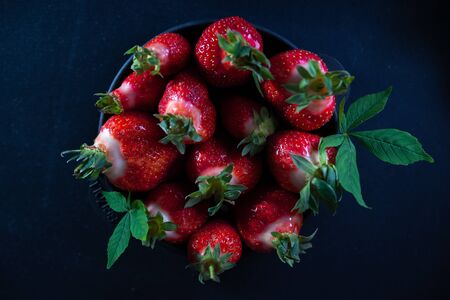 Fresh juicy strawberries in a black plate on a black matte background.の写真素材