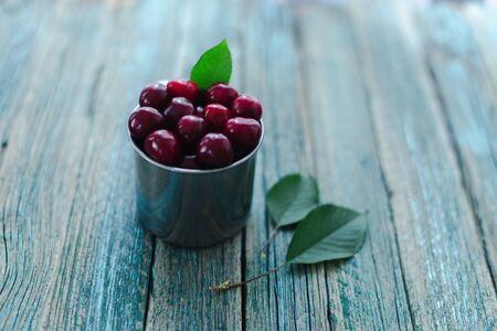 Cherries in a steel mug on a wooden background.の写真素材