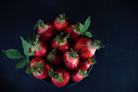 Fresh juicy strawberries in a black plate on a black matte background.の写真素材