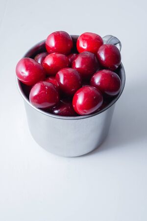 Sweet cherries in a steel mug on a white paper background.の写真素材