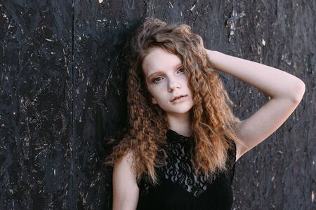 Red-haired girl in a black dress near a dark textured wall.の写真素材