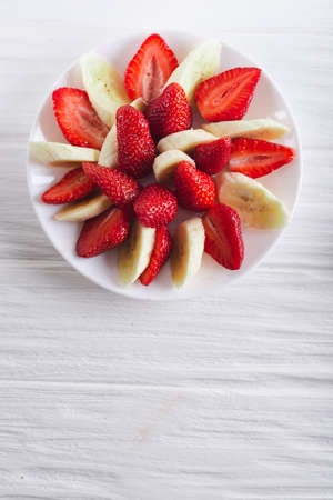 Juicy fresh sliced strawberries with banana on a white plate on a white wooden background.の写真素材