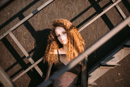Red-haired girl in a black dress near a dark textured wall.