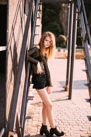 Red-haired girl in a black dress near a dark textured wall.の写真素材