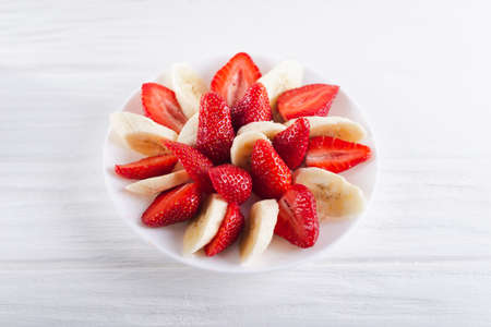Juicy fresh sliced strawberries with banana on a white plate on a white wooden background.の写真素材