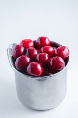 Sweet cherries in a steel mug on a white paper background.の写真素材