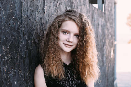 Red-haired girl in a black dress near a dark textured wall.の写真素材