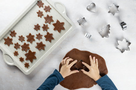 A child cuts a gingerbread cookie with a cookie cutter a snowflakes on a white background. Little...