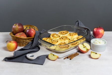 Freshly baked cinnabon buns in a shape stand on a white wooden table. Around are apples, showing whats in the filling. Above is a great place for text or recipe.の写真素材