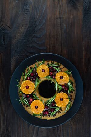 Tangerine ring cake decorated with sliced mandarines, cranberries and rosemary. Flat lay on wooden background.の写真素材