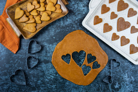 Making a gingerbread cookies, with a cutters shape of hearts. Beside is a baking tray and a wooden...