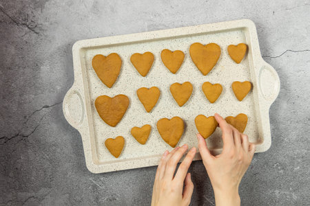 A womens hands hold a gingerbread a heart cookie on a concrete background with a baking tray. Flat lay cooking.の写真素材