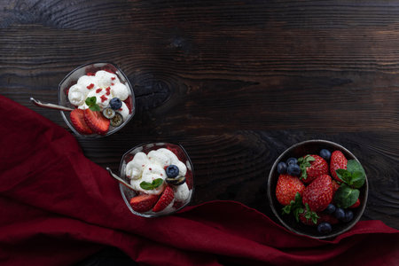 Two cream dessert in a glass with fresh berries, strawberries, blueberries. Flat lay on a dark wooden table with copy space.の写真素材