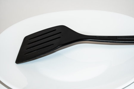 Black plastic kitchen spatula on white plateの写真素材