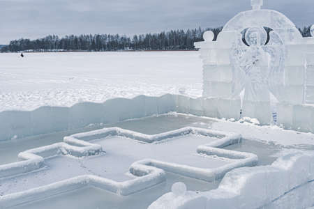 Font for dipping into an ice hole for the baptism of christ and ice sculpture in the form of an angel and a crossの写真素材