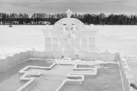 Font for dipping into an ice hole for the baptism of christ and ice sculpture in the form of an angel and a crossの写真素材