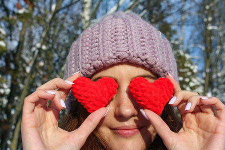 Valentines day, girl covers her eyes with knitted red hearts as a symbol of love