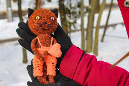 Knitted toy cat with an orange heart in handsの写真素材