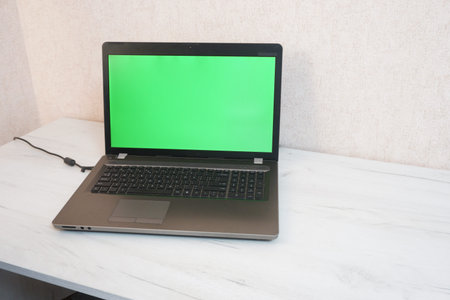 A laptop with a green screen stands on a white table, copy space