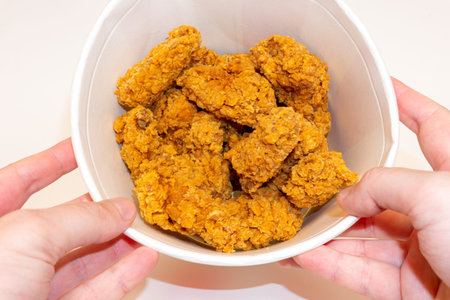 Deep fried spicy chicken wings in a crispy breading in a basket in hands, chicken fast food isolated...