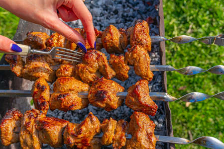 A girl using a fork checks the readiness of the kebab marinated meat on skewers on the grillの写真素材