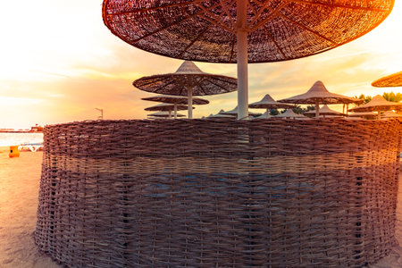 Straw Umbrella with wind fences in the sunset. Beach umbrellas, view of the beautiful blue and purple sunset, sky and straw beach umbrellas. Perfect holiday concept. Travel and holidays.の写真素材