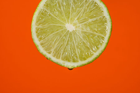 Water falling from green hue lime on red background. Lime slice and water splashing, drops of juice...