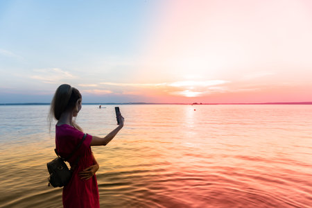 Girl silhouette watches the sunset while standing knee-deep in the water and in distance a jet ski...