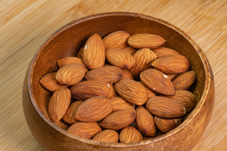Almond nuts in wooden bowl on wooden background close up. Product rich in minerals and vitamins. Almond kernels. Healthy skin and hair and natural healing oil treatmentの写真素材