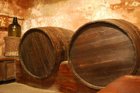 Two old wooden barrels in cellar with old brown walls and big green bottle in corner