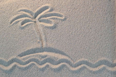 The island with palm tree in the sea is drawn on sandの写真素材