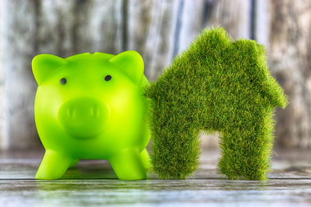 Piggy bank and miniature green eco house icon with grass on wooden background. Renewable energy concept. Energy saving in the household.の写真素材