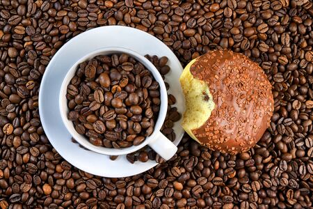 White porcelain cup, delicious donut with chocolate and whole coffee grains background. A coffee break. Conceptual image for lovers of delicious coffee.の写真素材
