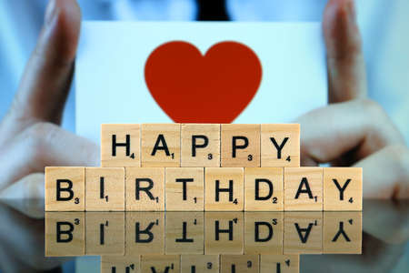WROCLAW, POLAND - FEBRUARY 28, 2020: The words HAPPY BIRTHDAY made of scrabble letters, and man holding a business card with a red heart symbol in the background. Studio shot.のeditorial素材
