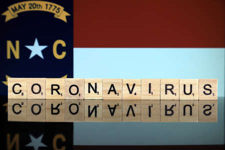 WROCLAW, POLAND - MARCH 28, 2020: Word CORONAVIRUS made of wooden letters, and North Carolina Flag in the background. Coronavirus (COVID-19) global disease 2020.のeditorial素材