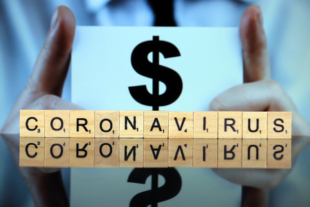 WROCLAW, POLAND - MARCH 30, 2020: The word CORONAVIRUS made of wooden letters, and man holding a business card with dollar symbol in the background. Coronavirus (COVID-19) global disease 2020.のeditorial素材