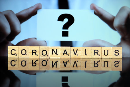 WROCLAW, POLAND - MARCH 30, 2020: The word CORONAVIRUS made of wooden letters, and man holding a business card with question mark in the background. Coronavirus (COVID-19) global disease 2020.のeditorial素材
