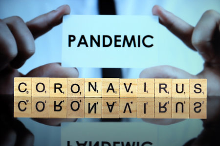 WROCLAW, POLAND - MARCH 30, 2020: The word CORONAVIRUS made of wooden letters, and man holding a business card with the word PANDEMIC in the background. Coronavirus (COVID-19) global disease 2020.のeditorial素材