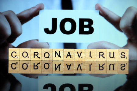 WROCLAW, POLAND - MARCH 30, 2020: The word CORONAVIRUS made of wooden letters, and man holding a business card with the word JOB in the background. Coronavirus (COVID-19) global disease.のeditorial素材