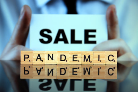WROCLAW, POLAND - MARCH 30, 2020: The word PANDEMIC made of wooden letters, and man holding a card with the word SALE in the background. Coronavirus (COVID-19) global disease 2020.のeditorial素材