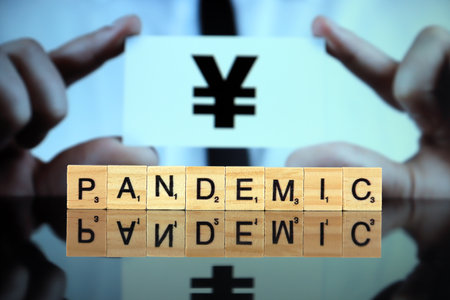 WROCLAW, POLAND - MARCH 30, 2020: The word PANDEMIC made of wooden letters, and man holding a business card with yen or yuan sign in the background. Coronavirus (COVID-19) global disease 2020.のeditorial素材